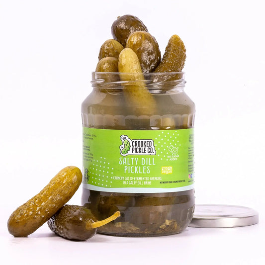 Jar of Crooked Pickle Co. salty dill lacto-fermented pickles with fresh dill and crunchy textures in a clear glass jar.