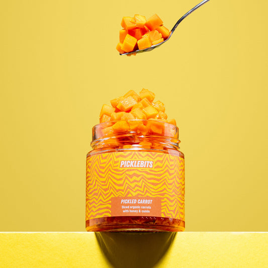 Jar of organic pickled carrot chopped with spoon on yellow background