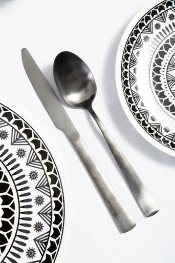 Onyx 16-piece cutlery set by Avie, including knives, forks, and spoons, displayed on a wooden table.