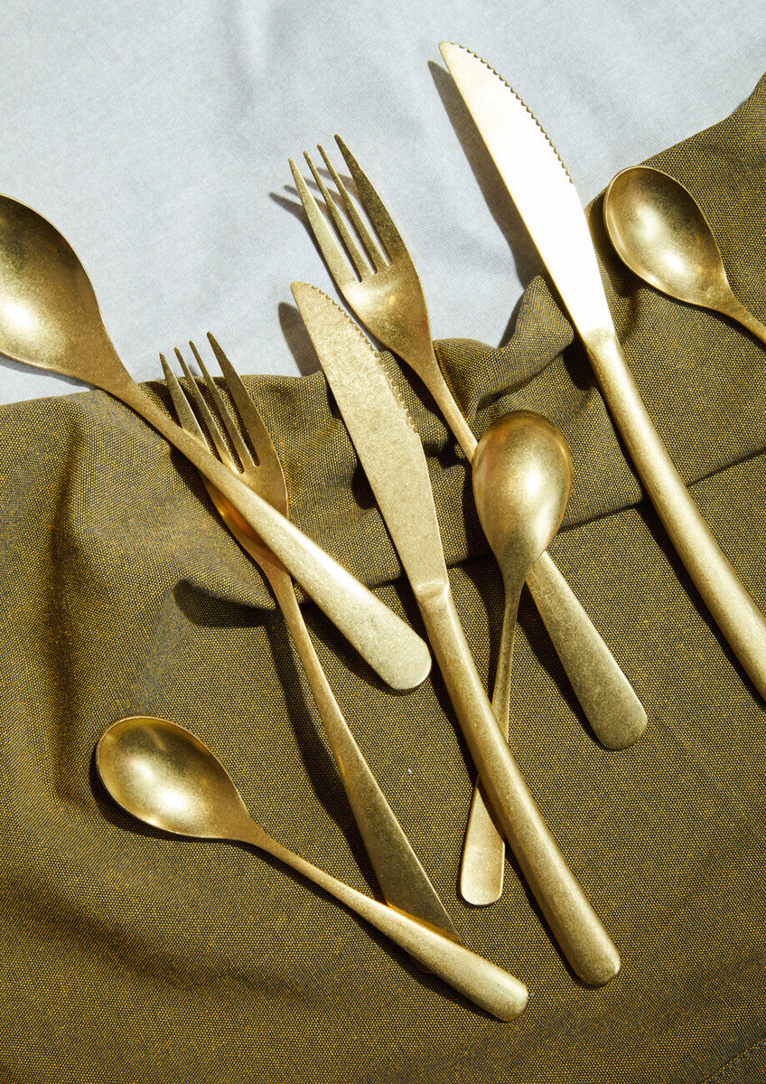 16-piece antique gold finish cutlery set by Orsina, featuring forks, knives, spoons, and serving utensils arranged on a wooden surface.