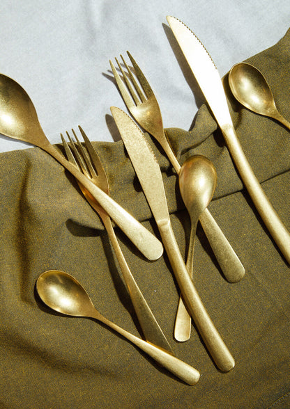 16-piece antique gold finish cutlery set by Orsina, featuring forks, knives, spoons, and serving utensils arranged on a wooden surface.