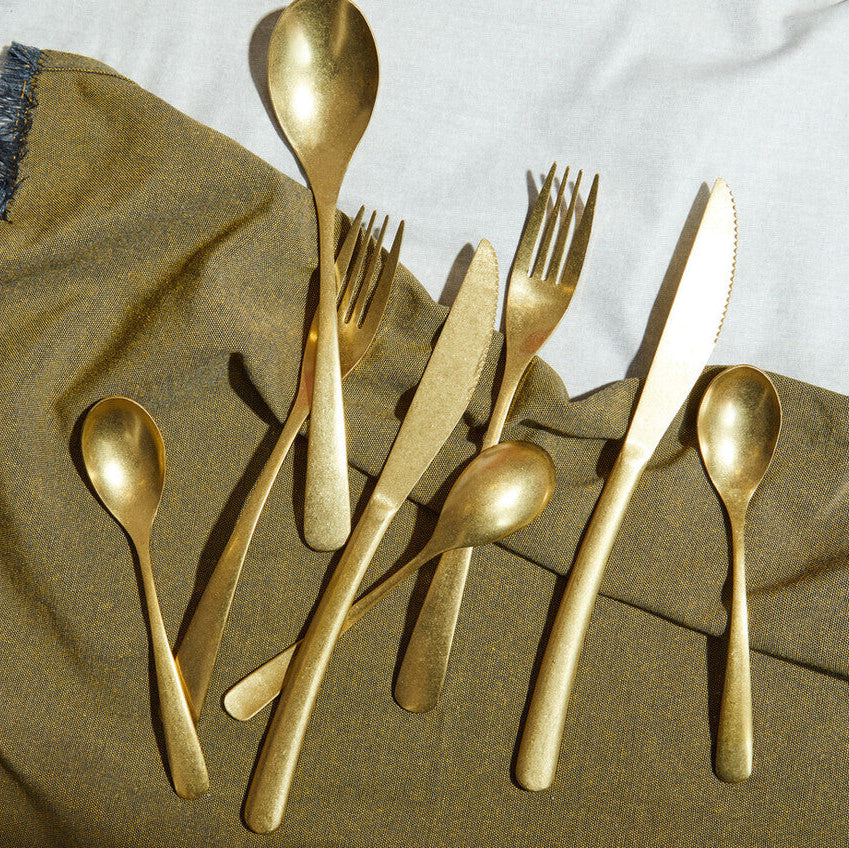 Orsina 16-piece antique gold finish cutlery set with forks, knives, and spoons arranged on a wooden table.