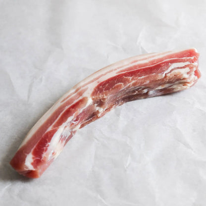 Thinly sliced smoked streaky bacon from Primrose Herd, dry cured, with visible marbling and crispy edges on a white background.