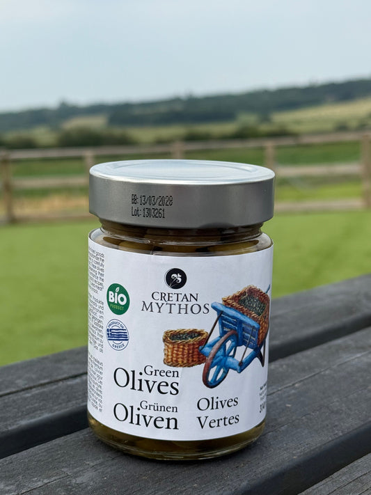 Organic Greek green olives in brine from Cretan Mythos, displayed in a clear jar with olives and herbs visible inside.