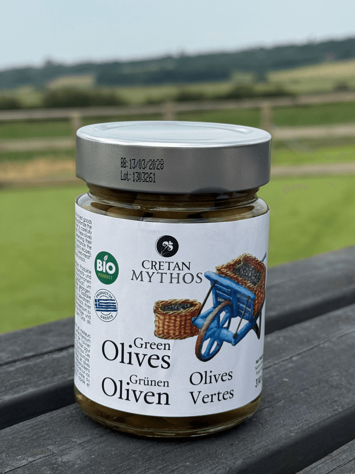 Organic Greek green olives in brine from Cretan Mythos, showcased in a glass jar with fresh herbs and olives visible inside.