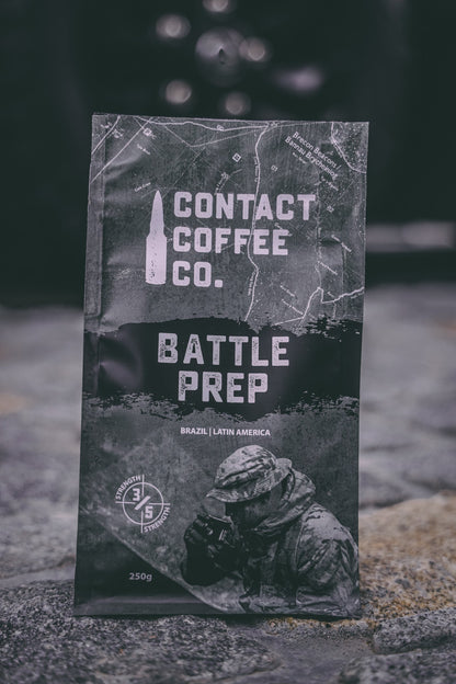 A cup of Battle Prep Coffee by Contact Coffee Company Ltd. with a steaming hot coffee beverage in a white mug on a wooden table.