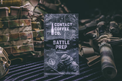 A cup of Battle Prep Coffee from Contact Coffee Company Ltd. on a wooden table, showing a steaming coffee beverage in a branded mug.