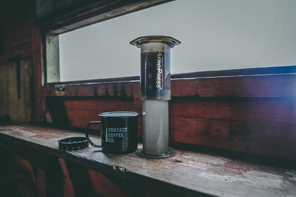 AeroPress Travel Coffee Maker by Contact Coffee Company Ltd., compact portable coffee brewing gear on a clean surface.