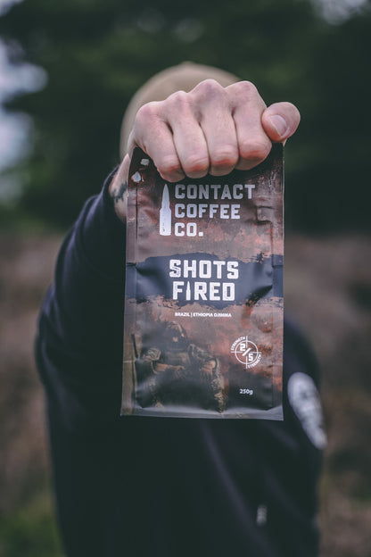 A bag of Shots Fired Coffee by Contact Coffee Company Ltd., featuring a dark roasted coffee bean design on the packaging.