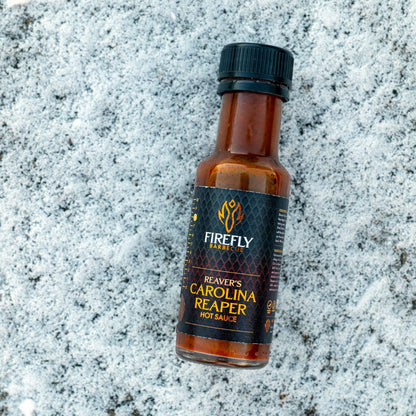 FireFly Barbecue Carolina Reaper hot chili sauce bottle on a rustic wooden surface, showcasing fiery red sauce with Reaper peppers.