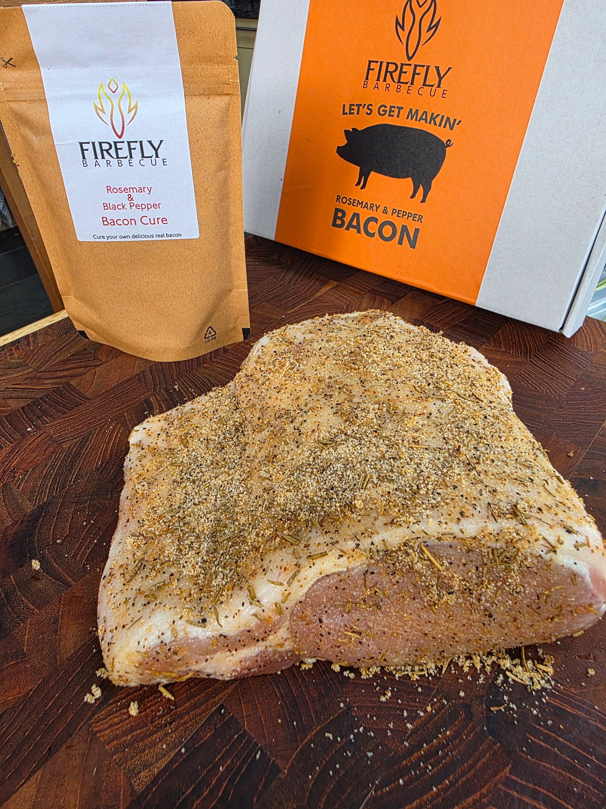 FireFly Barbecue Bacon Curing Kit with rosemary and black pepper, featuring curing salts, spices, and tools for homemade bacon.