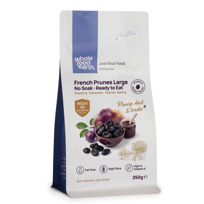 Whole Food Earth large dried French prunes, no soak needed, in a clear container, showcasing their dark, wrinkled appearance.