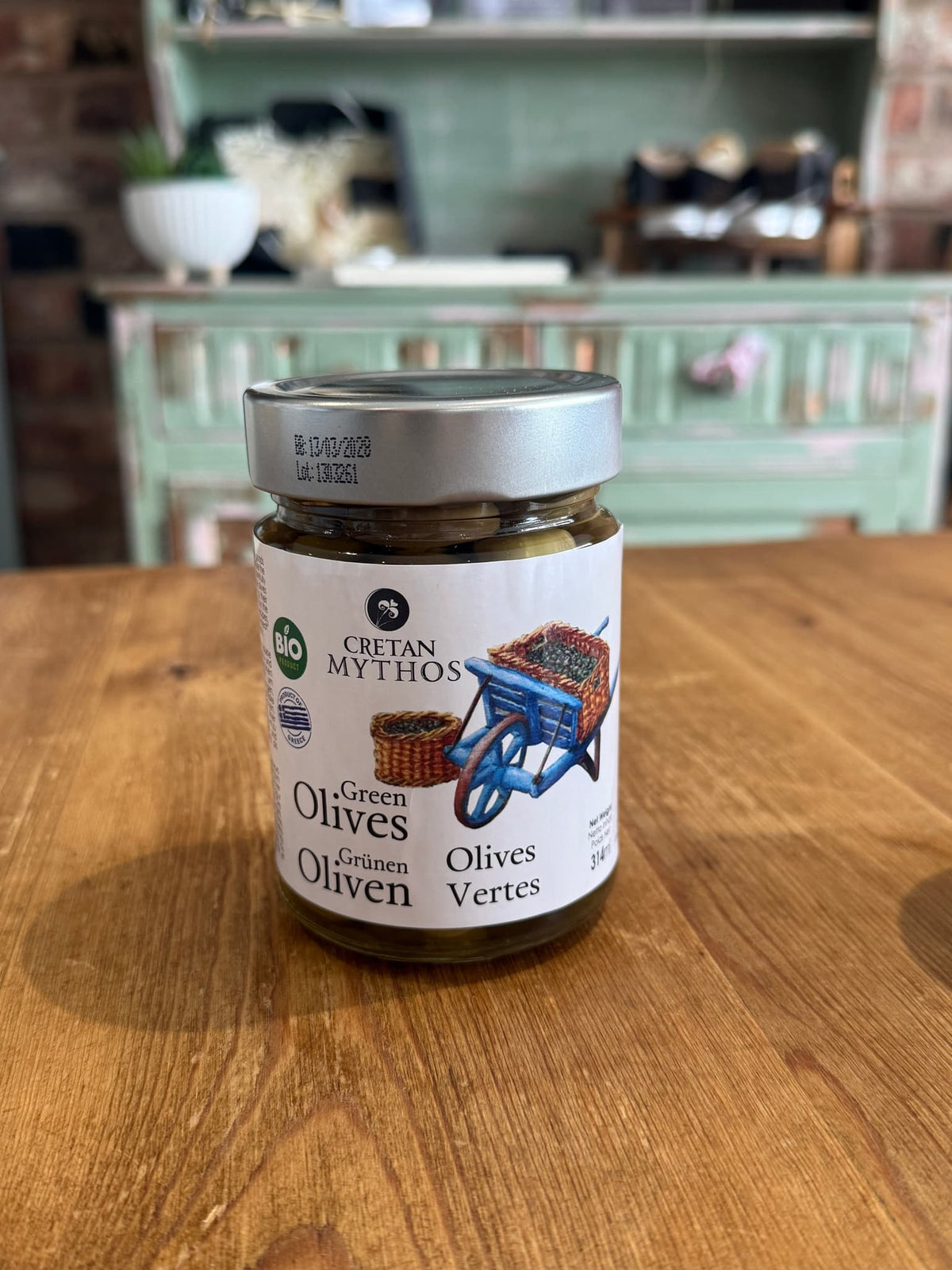 Organic Greek green olives in brine from Cretan Mythos, displayed in a glass jar on a wooden surface.