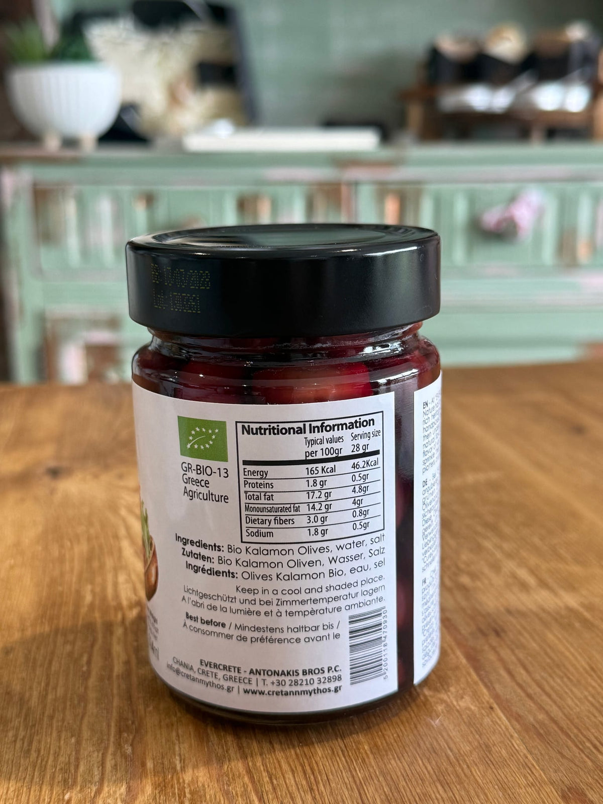 Organic Kalamata olives in brine from Cretan Mythos, Greek Olives, shown in a glass jar with dark purple olives and green herbs.