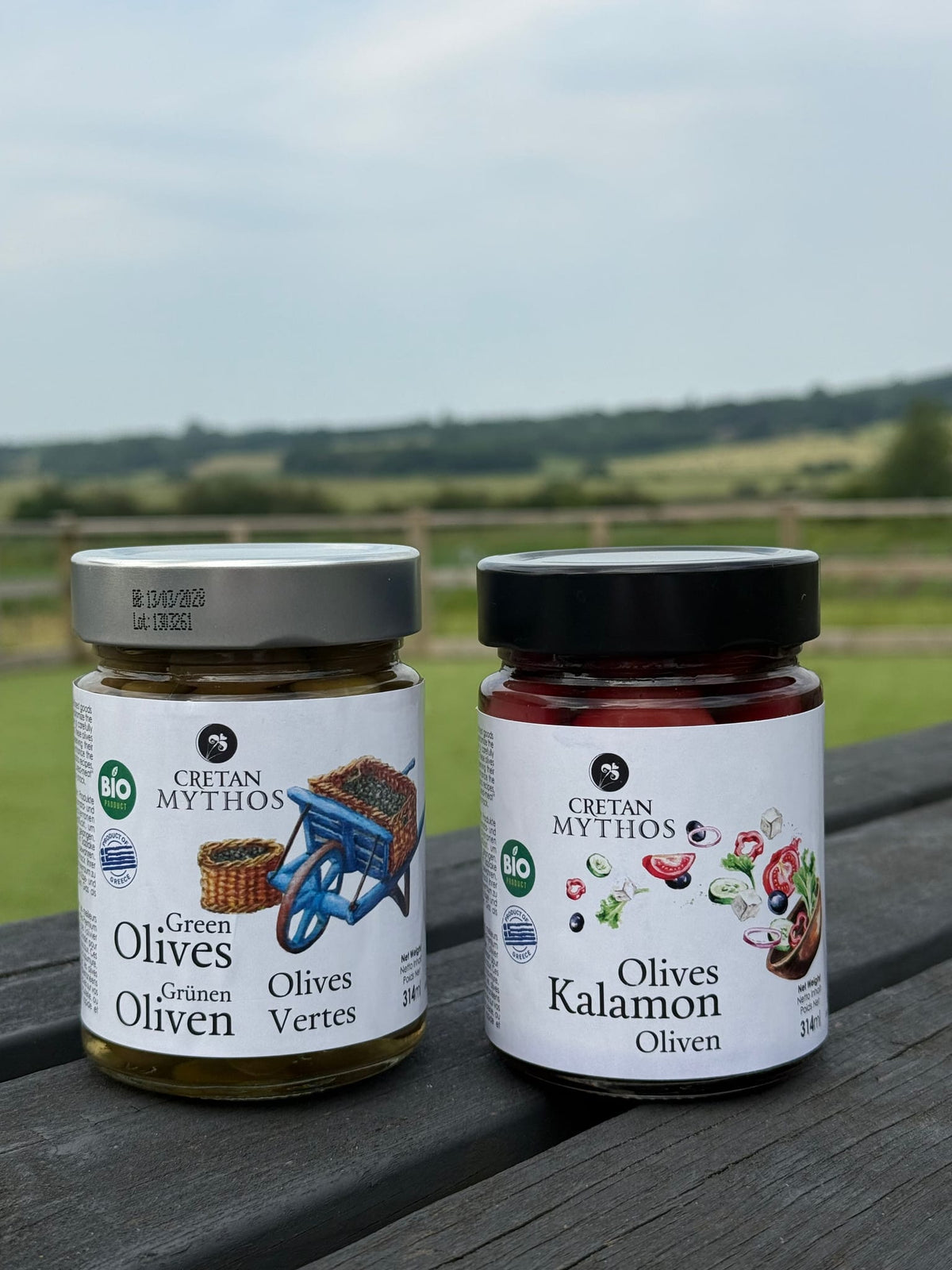 Greek organic Kalamata olives in brine from Cretan Mythos, shown in a clear glass jar with dark, shiny olives inside.