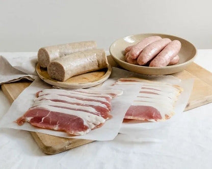 Primrose Herd Cornish breakfast hamper with assorted meats, including sausages, bacon, and cured meats, arranged in a rustic box.