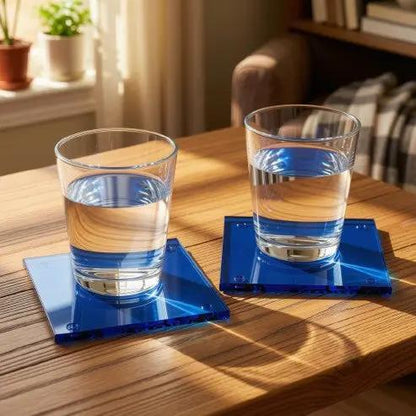 Blue glass square coaster from Glassware UK, shown on a wooden table with nearby accessories and a drink.