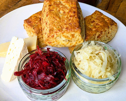 Close-up of a cheese scone on a plate, highlighting its golden-brown crust and crumbly texture, by Cultura Live Food.