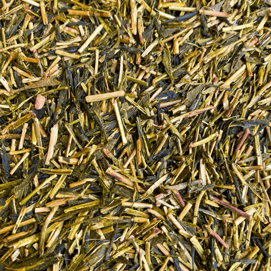 Fresh green Kukicha tea leaves from Porter Hill Tea Company, displayed in a clear glass jar on a wooden surface.