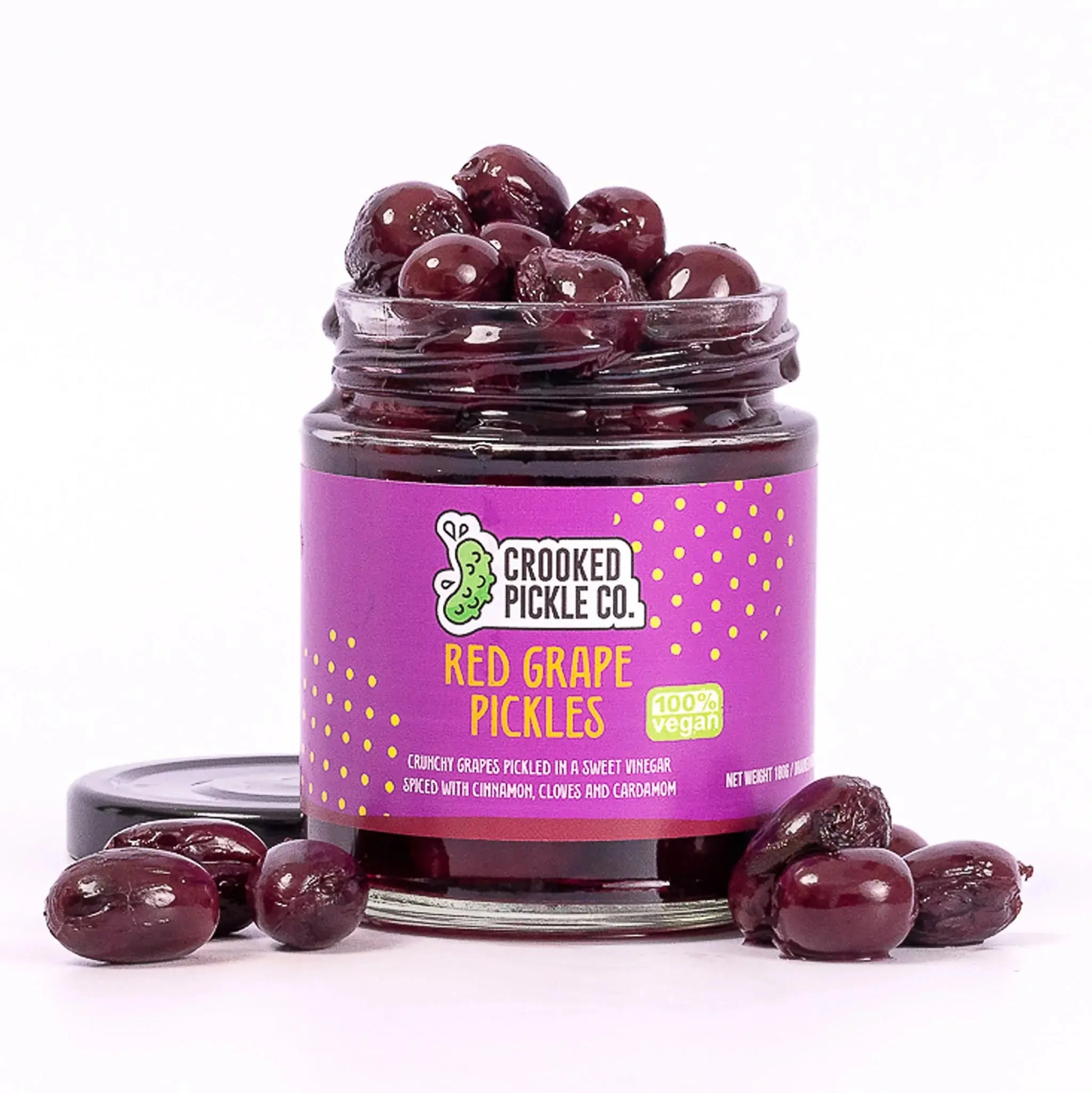 A jar of Crooked Pickle Co. red grape pickles with stacked bright red grapes and pickles inside, on a rustic wooden surface.