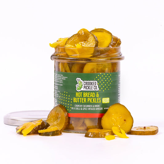 Jar of Crooked Pickle Co. hot bread and butter pickles with sliced cucumbers and spices in a clear glass jar on a white background.
