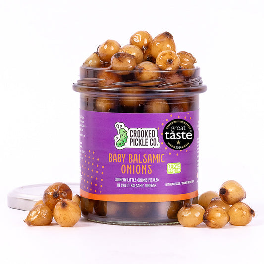 Jar of Crooked Pickle Co Baby Balsamic Onions with a label showing the product name and brand on a wooden surface.