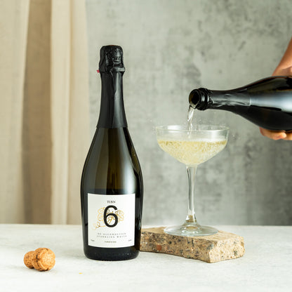 Six bottles of Turn 6 alcohol-free sparkling white and red wine in a case, featuring elegant labels and vibrant colors.