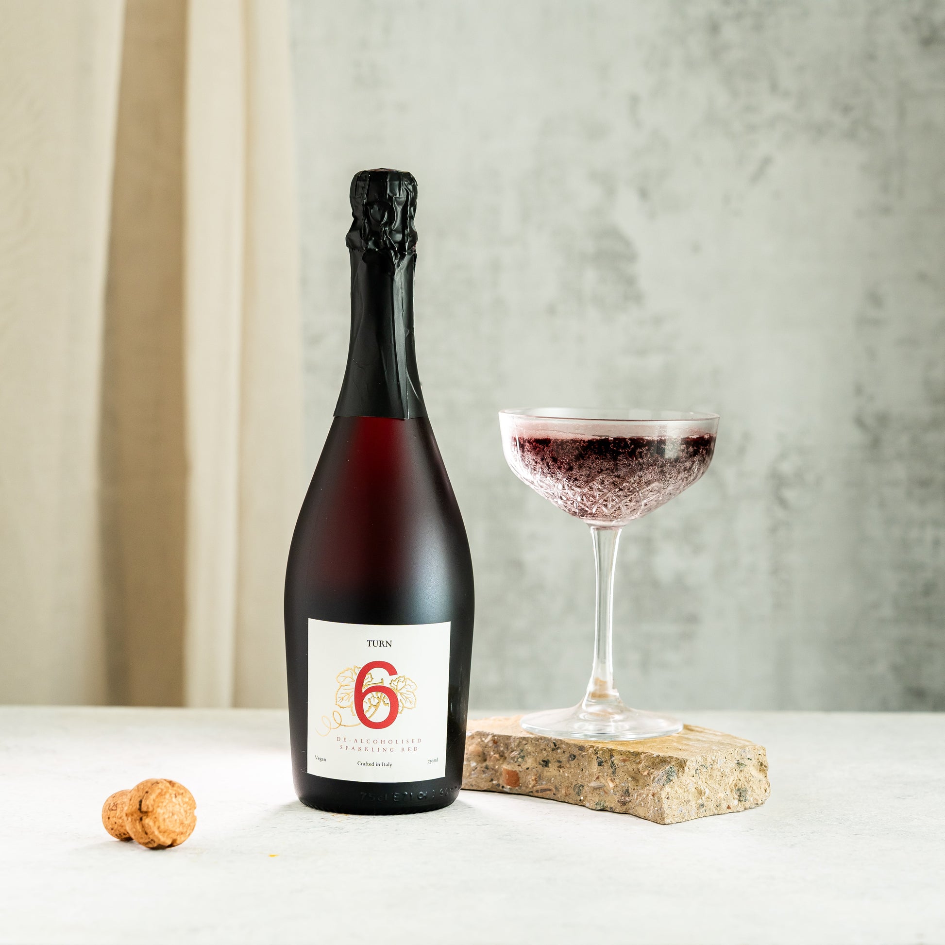 Six bottles of Turn 6 alcohol-free sparkling red wine in a case, showcasing vibrant red color and elegant glass bottles.