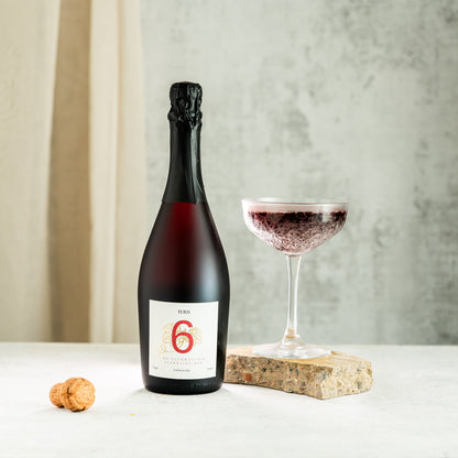 Six bottles of Turn 6 alcohol-free sparkling red wine in a case, showcasing vibrant red color and elegant glass bottles.