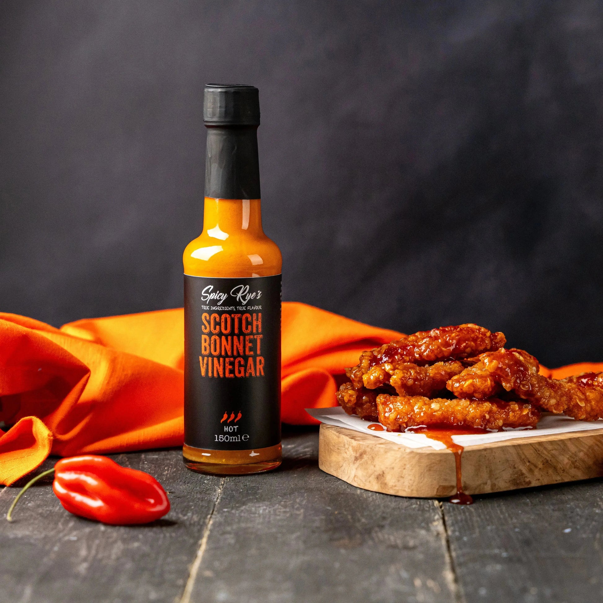 Spicy Ryes Scotch Bonnet vinegar bottle with label, showcasing the fiery red hot peppers used in the hot sauce product.