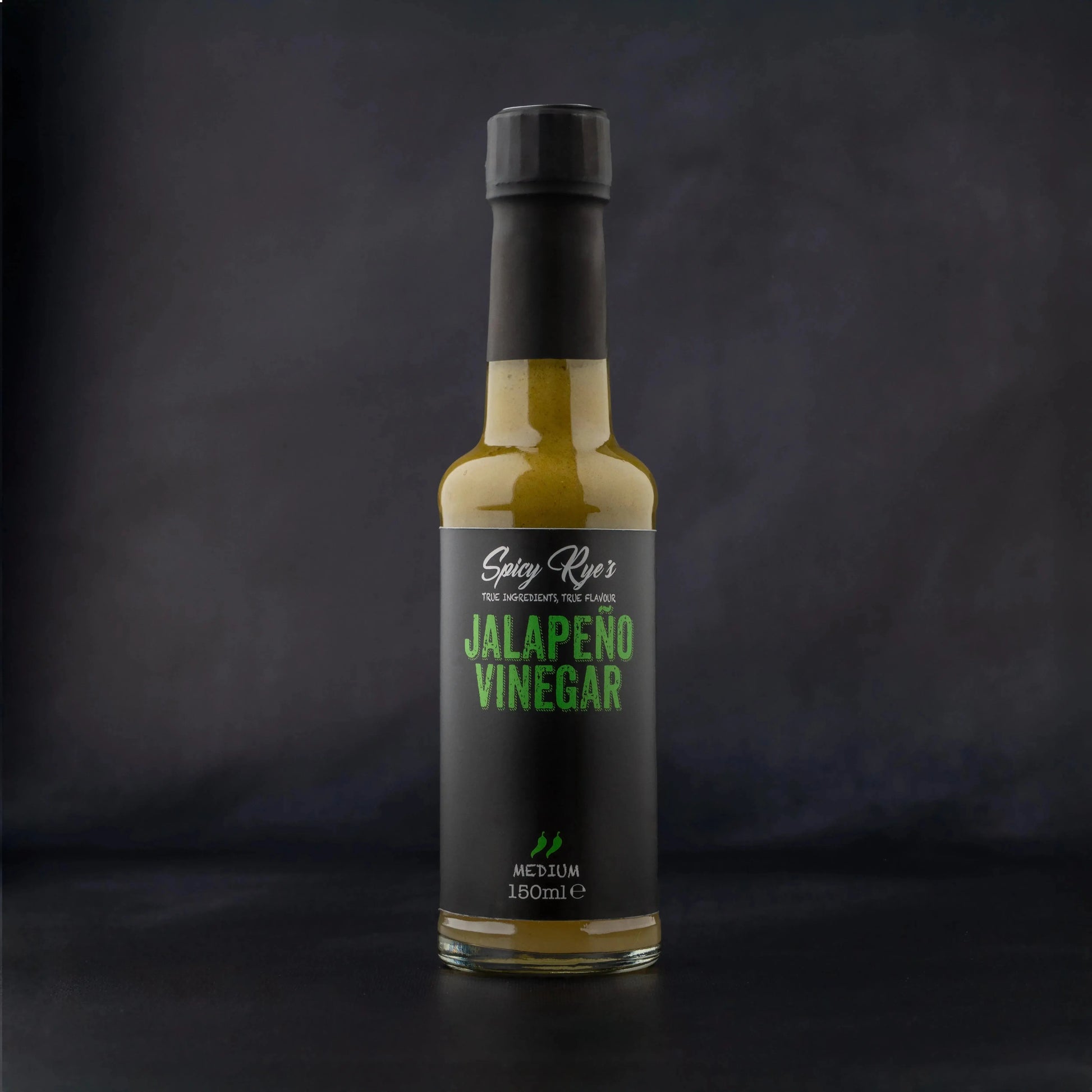 Spicy Ryes Jalapeño Vinegar bottle with vibrant green jalapeño peppers and clear liquid, on a rustic wooden surface.
