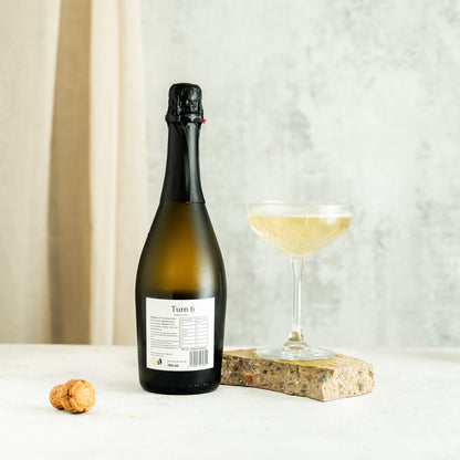 Glass of Turn 6 alcohol-free sparkling white wine with a golden hue and bubbles, served in a clear flute.