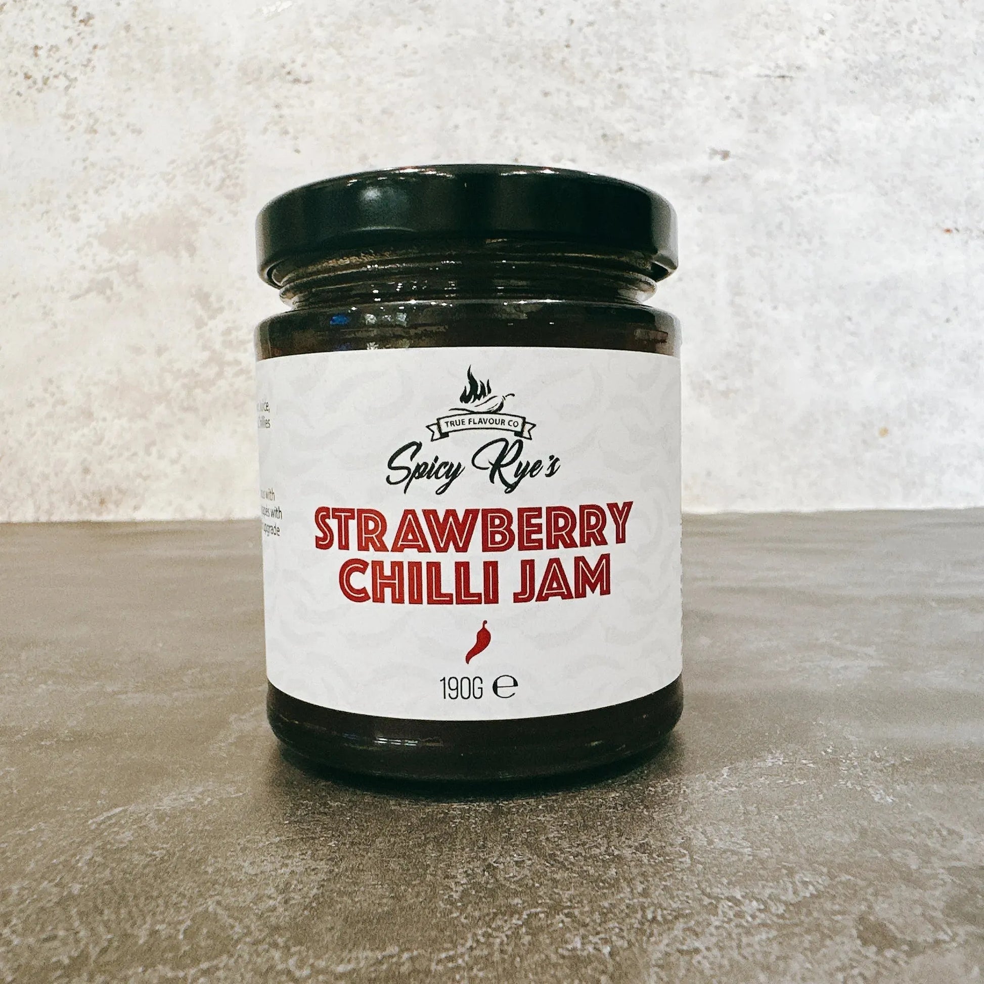 Jar of Spicy Ryes Strawberry Chilli Jam with fresh strawberries and red chili peppers on the label.
