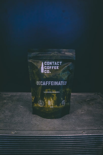 Decaffeinated coffee from Contact Coffee Company Ltd., showing a brewed cup with coffee beans and a coffee bag on a wooden table.