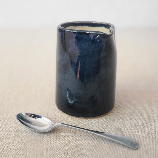 Jet black small ceramic jug with a matching spoon, designed by Katie L Thompson Designs, perfect for serving and decorative use.