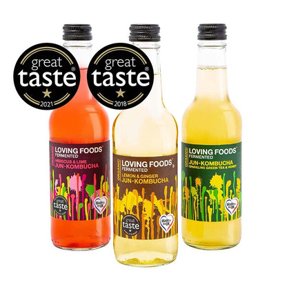 Assorted bottles of Loving Foods Organic Jun-Kombucha in a mixed case, featuring colorful labels and glass bottles on a wooden surface.