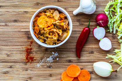 Organic Loving Foods Kimchi ingredients including cabbage, radish, garlic, and chili peppers on a wooden surface.