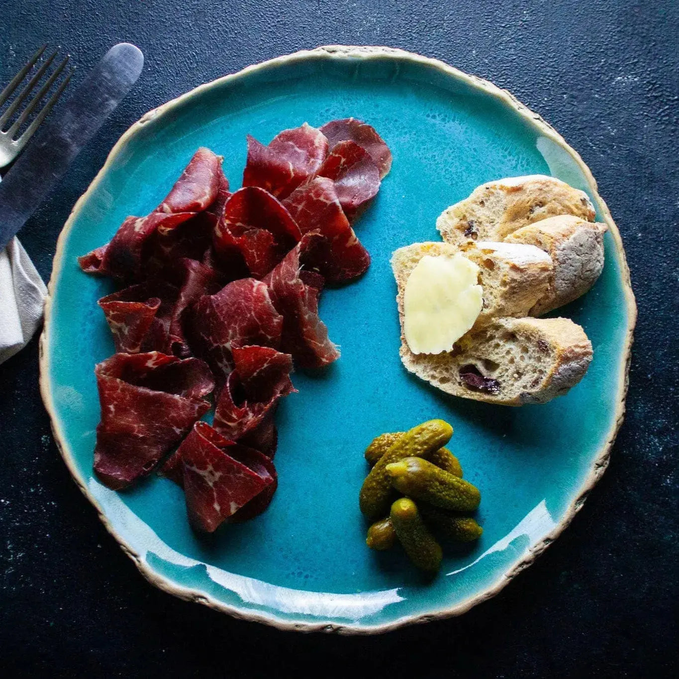 Thin slices of London Smoke & Cure Bresaola, a premium artisan charcuterie, displayed on a wooden board with herbs and cheese.