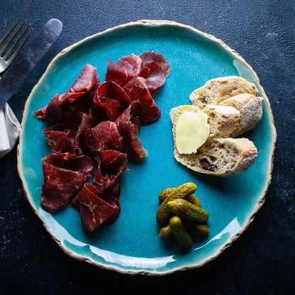 Thin slices of London Smoke & Cure Bresaola, a premium artisan charcuterie, displayed on a wooden board with herbs and cheese.