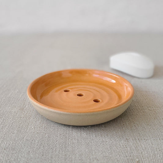 Mandarin orange ceramic soap dish by Katie L Thompson Designs with a classic round shape and vibrant orange color.