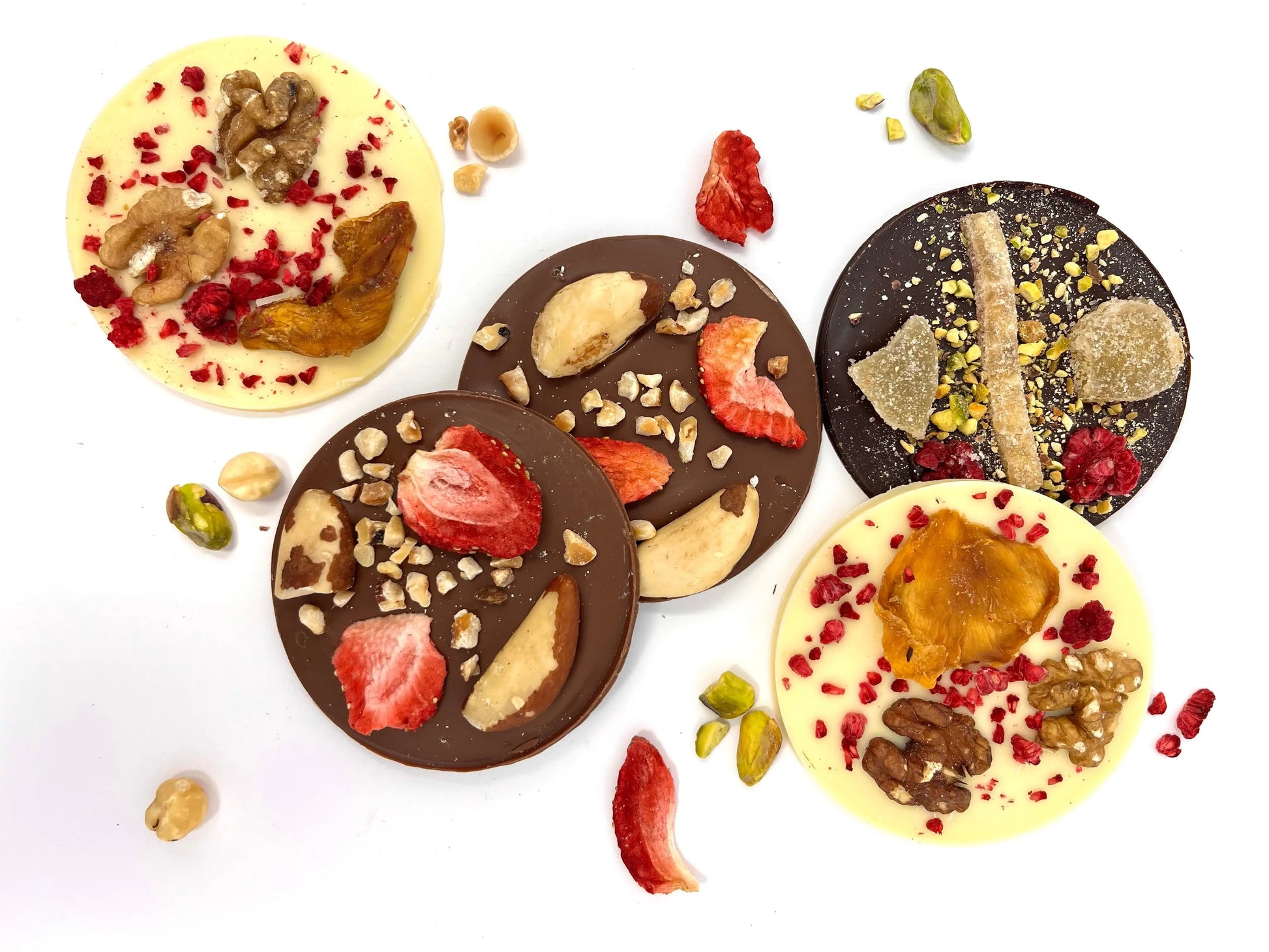 Assorted Gorvett & Stone dark chocolate mendiants with dried fruits and nuts arranged on a white plate.