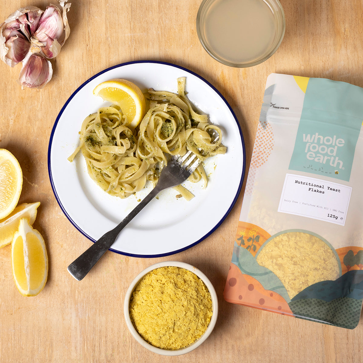 Whole Food Earth nutritional yeast flakes (Nooch) with B12 in a jar, shown alongside a bowl of prepared food on a kitchen counter.
