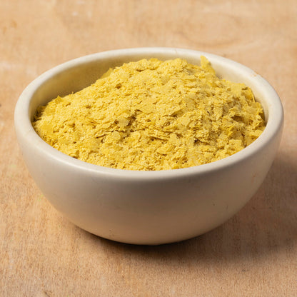 Whole Food Earth nutritional yeast flakes with B12 in a kitchen setting, showing the flaky yellow supplement for nuts and seeds.