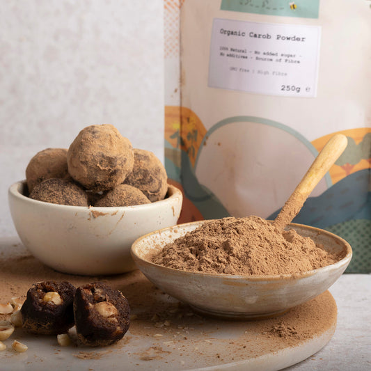 Organic Carob Powder by ArtisanBox in a natural setting, showcasing the fine, dark powder in a rustic bowl with a spoon.