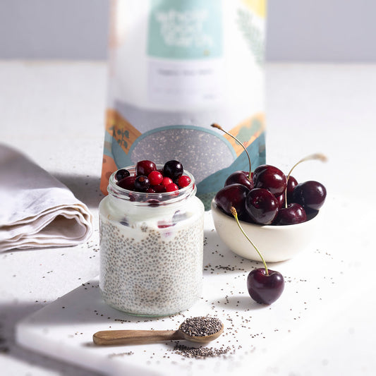 Organic chia seeds in a glass bowl with a spoon, showcasing the fresh, nutrient-rich seeds from ArtisanBox on a wooden surface.