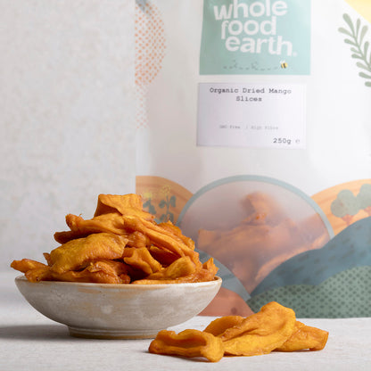 Organic dried mango slices from Whole Food Earth, shown in a natural setting with fresh mango pieces and dried fruit on a wooden surface.