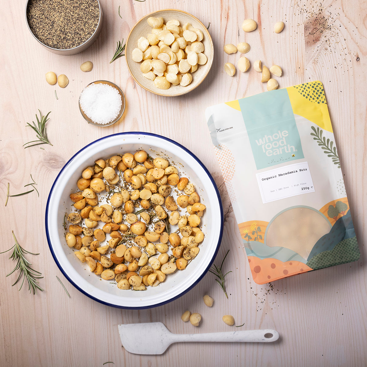 A bowl of Whole Food Earth organic macadamia nuts with whole nuts and cracked shells, on a wooden surface.
