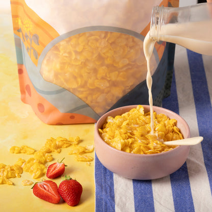 Bowl of organic natural corn flakes cereal on a wooden table with milk and fresh fruit, showcasing Whole Food Earth brand.