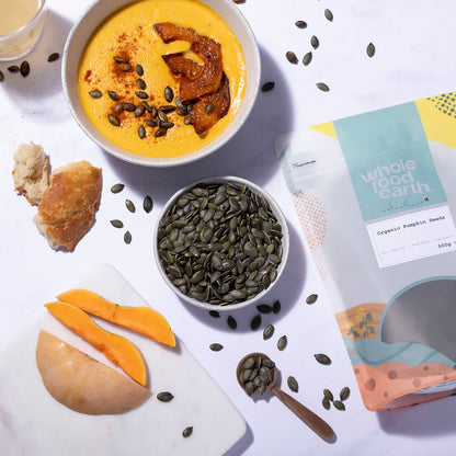 Organic pumpkin seeds from Whole Food Earth, displayed in a bowl with fresh pumpkins in the background.