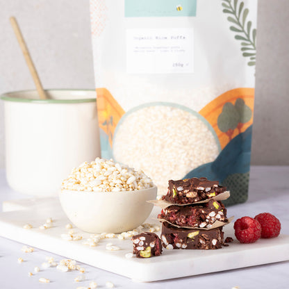 Organic Rice Puffs from Whole Food Earth, showing a bowl of crispy rice cereal on a wooden table with a spoon and fresh fruit.